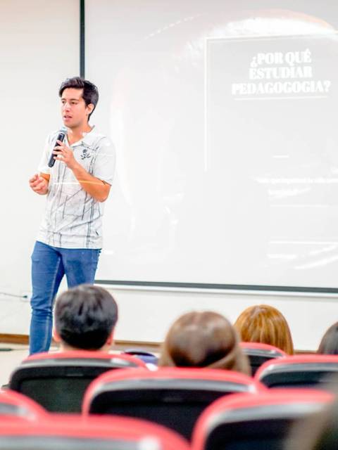 Un presentador está hablando frente a una audiencia durante un evento académico.