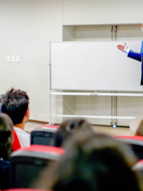 Un ponente habla frente a una audiencia en un salón de conferencias.