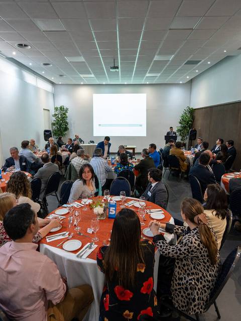 Una sala de conferencias con varias mesas y personas sentadas alrededor en un ambiente de reunión.