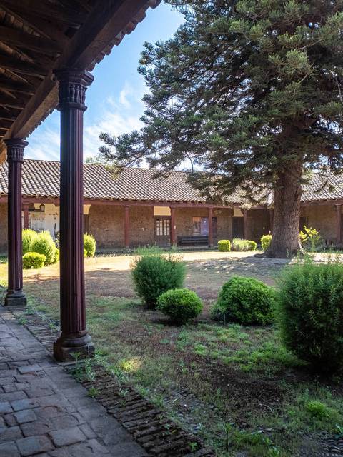 Un pasillo con columnas que da a un jardín con árboles y arbustos.