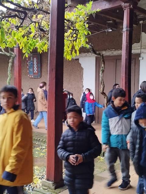Un grupo de niños camina por un pasillo cubierto, rodeado de vegetación y paredes de barro.