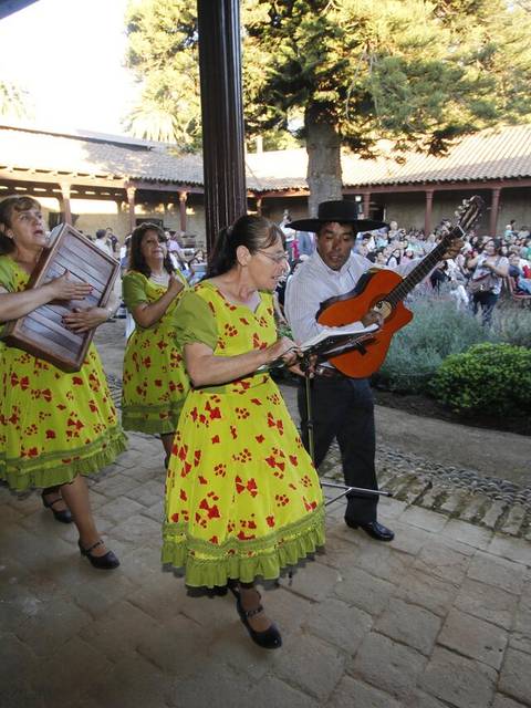 Un grupo de músicos con vestidos coloridos caminan mientras tocan instrumentos en un evento al aire libre.