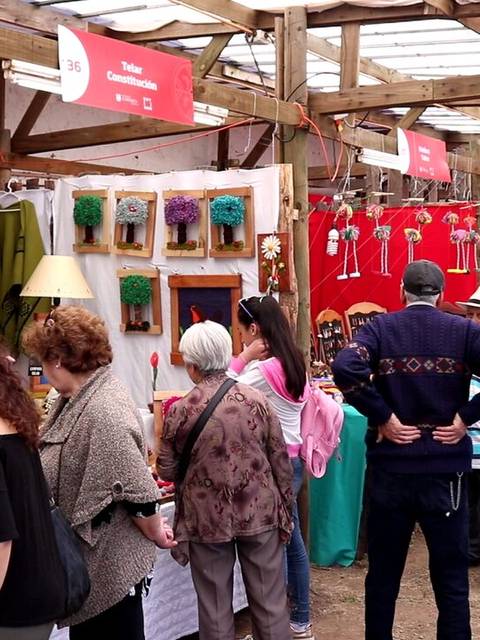 Una feria de artesanías con varias personas observando y comprando productos artesanales.
