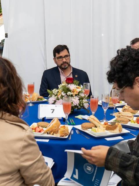 Un grupo de personas en una reunión sentadas alrededor de una mesa con comida y bebidas.