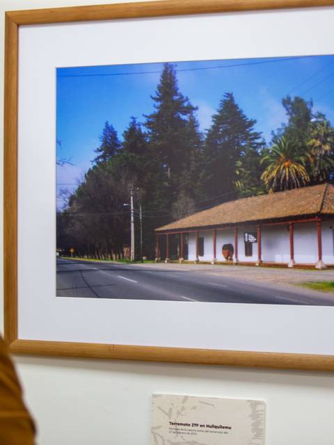 Una mujer observa una fotografía de una casa tradicional junto a un camino.