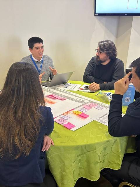 Un grupo de personas participa en una reunión alrededor de una mesa, discutiendo y trabajando en un proyecto.