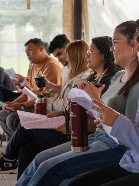 Un grupo de personas sentadas en la misma fila, cada una con sus papeles y botellas de agua en un ambiente compartido.