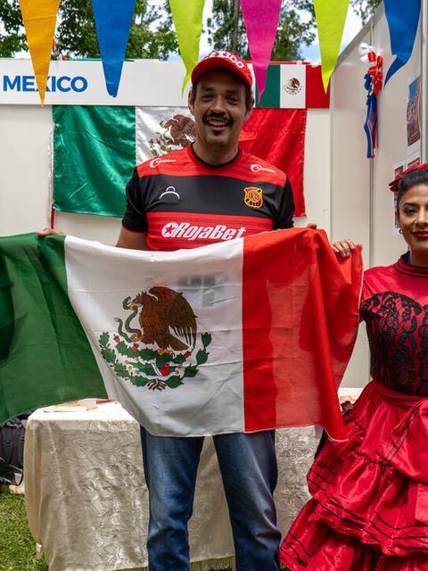 Tres personas vestidas con trajes tradicionales sosteniendo una bandera de México en un evento cultural.