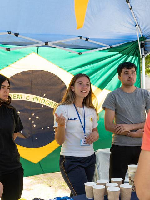 Un grupo de jóvenes interactuando en un evento con una bandera de Brasil de fondo.