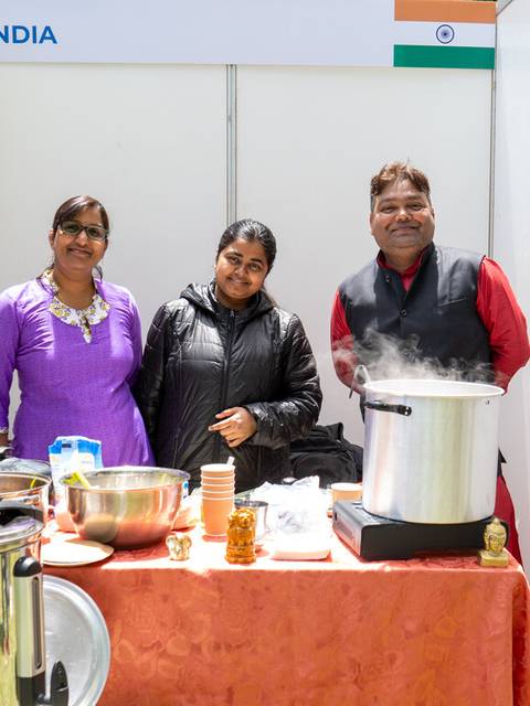 Tres personas posan en un stand que representa a India, rodeadas de utensilios de cocina y decoraciones.