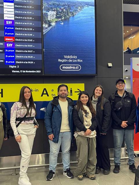Un grupo de personas se encuentra en el aeropuerto frente a un panel de llegadas y salidas.
