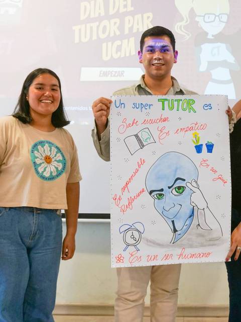 Tres personas posan con un cartel que describe las características de un buen tutor en un evento escolar.