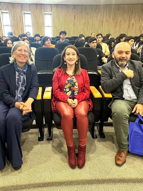 Tres personas sentadas en un auditorio con un público al fondo.