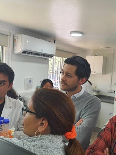 Un grupo de personas observa atentamente a un científico que presenta muestras en un laboratorio.