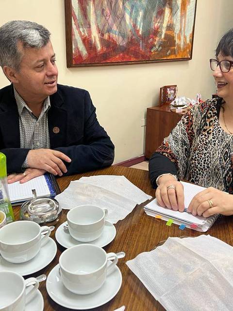 Una pareja de personas conversando en una mesa con varias tazas de café y utensilios a su alrededor.