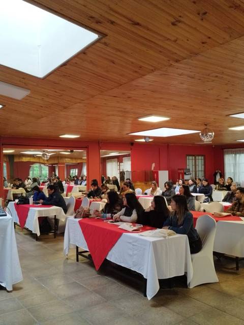Una sala con varias mesas y un grupo de personas atendiendo a una charla o presentación.