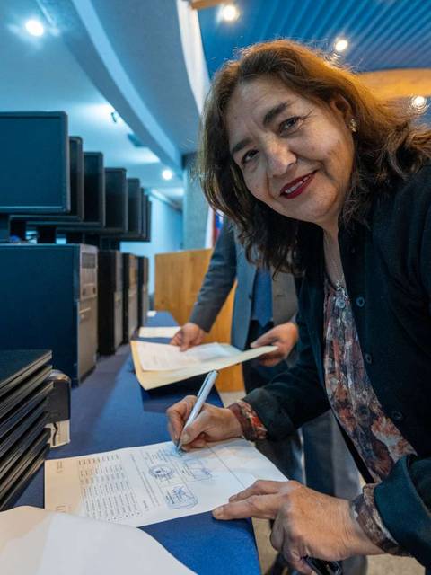 Una mujer sonriente está firmando un documento en un evento relacionado con tecnología.