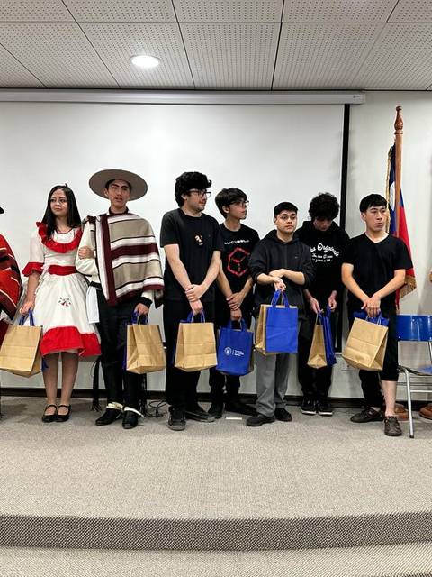 Un grupo de jóvenes vestidos con trajes típicos sonríen mientras sostienen bolsas en un evento formal.