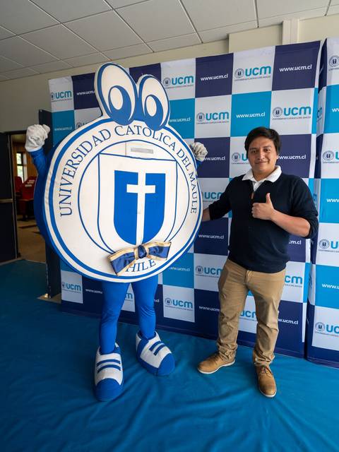 Un estudiante posa junto a una mascota de la Universidad Católica del Maule en un evento.