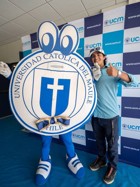 Un estudiante sonriente posa junto a la mascota de la Universidad Católica del Maule en un evento.