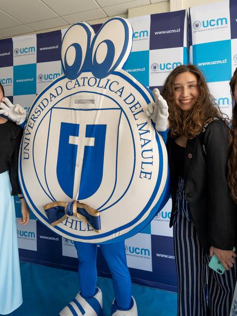 Tres jóvenes posan junto a un emblema de la Universidad Católica del Maule en un evento.