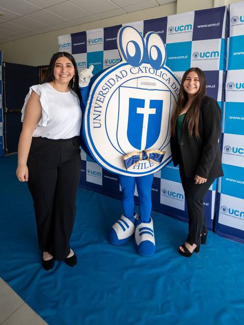 Dos mujeres posan junto a una mascota de la Universidad Católica del Maule en un evento.