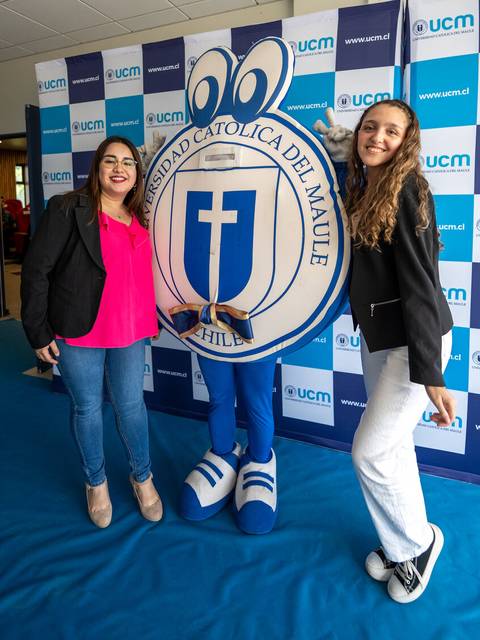 Dos mujeres posan junto a la mascota de la Universidad Católica del Maule en un evento.