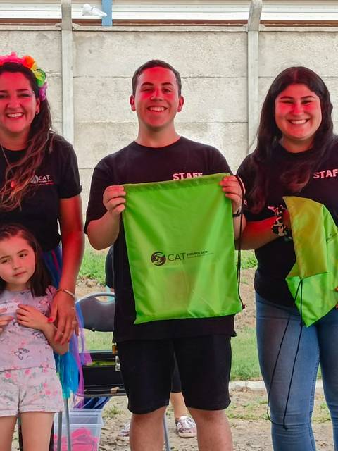 Un grupo de cuatro personas sonríe mientras sostienen bolsas verdes en un evento al aire libre.