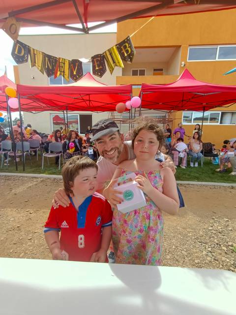 Una celebración al aire libre con un hombre sonriente y dos niños sosteniendo un objeto entre ellos.