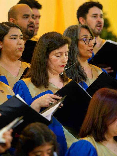 Un coro de personas cantando en un evento, vestidos con túnicas azules y doradas.