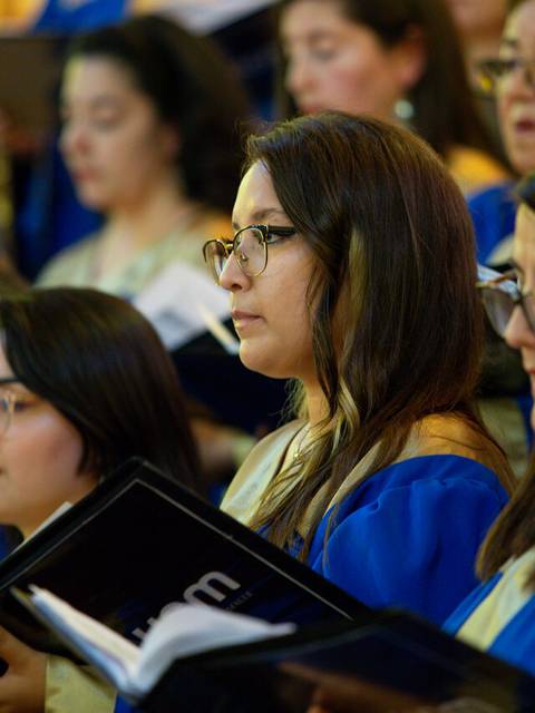 Un grupo de mujeres cantando en un coro, vestidas con batas azules y beige.