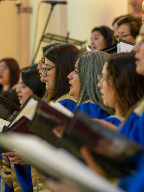 Un coro femenino canta con partituras en un escenario iluminado.