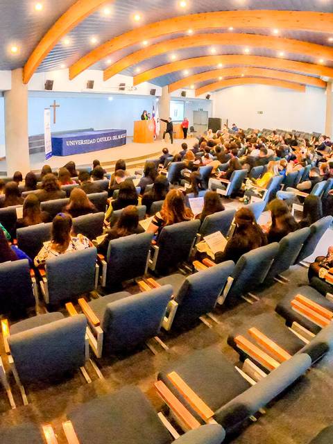 Una gran audiencia asiste a una conferencia en un auditorio con un escenario al fondo.