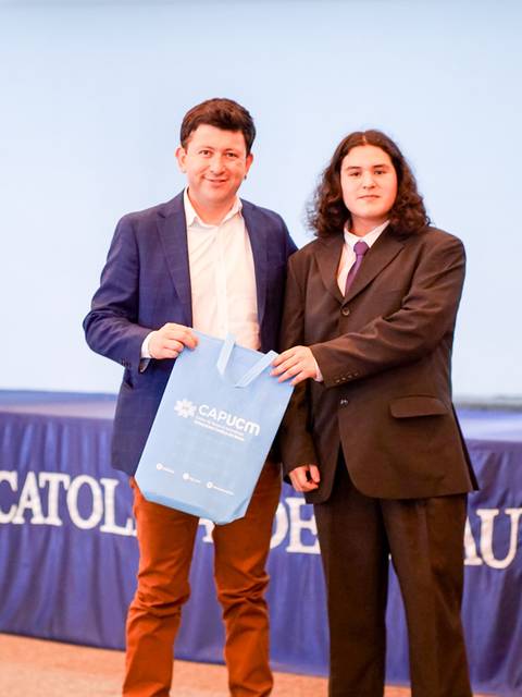 Un hombre entrega una bolsa a un joven durante un evento en la Universidad Católica de Maule.