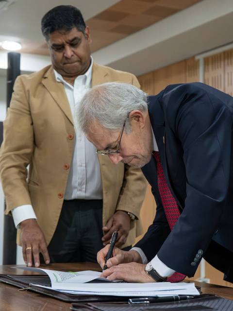 Dos hombres en una reunión, uno de ellos firmando un documento mientras el otro observa.