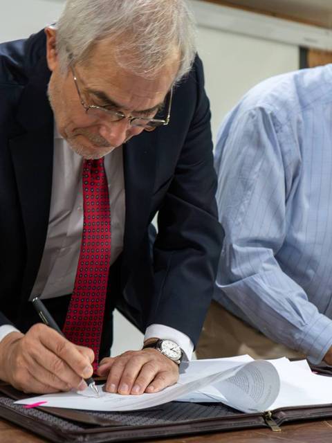 Dos hombres firmando documentos en una mesa.