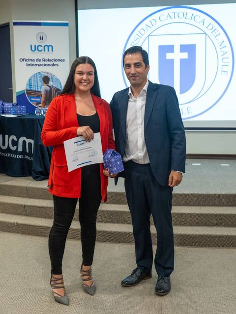 Una mujer y un hombre posan en un evento, la mujer sostiene un certificado y ambos sonríen.