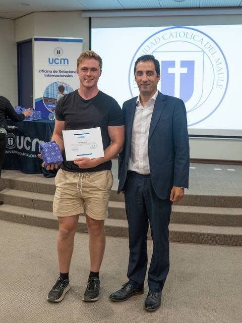 Un estudiante recibe un certificado y un premio en un evento formal de la universidad.
