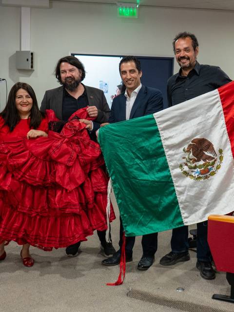 Un grupo de personas posando con una bandera de México y vestimenta tradicional en un evento.