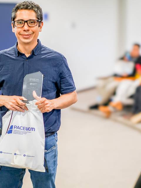 Un hombre sonriente sostiene un trofeo y una bolsa en un evento.