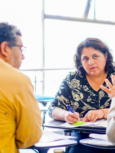 Un grupo de tres personas discute en una mesa mientras una mujer toma notas.