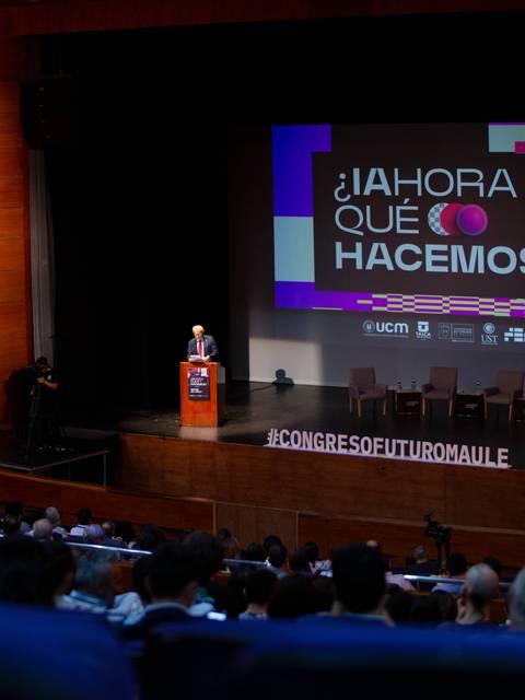 Un orador en un escenario durante un congreso con asistentes en la audiencia.