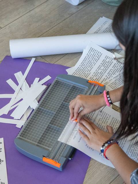 Una persona recorta papel utilizando una guillotina en un área con diversos materiales de manualidades.