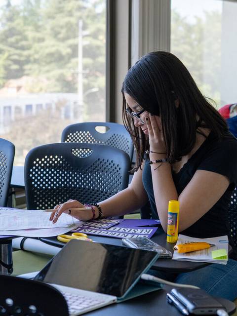 Una estudiante revisa documentos y materiales en un aula con luz natural.