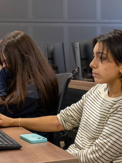 Una estudiante concentrada frente a una computadora en un aula.
