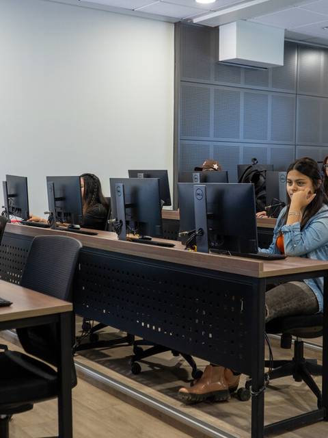 Un grupo de estudiantes sentados frente a computadoras en un aula moderna.