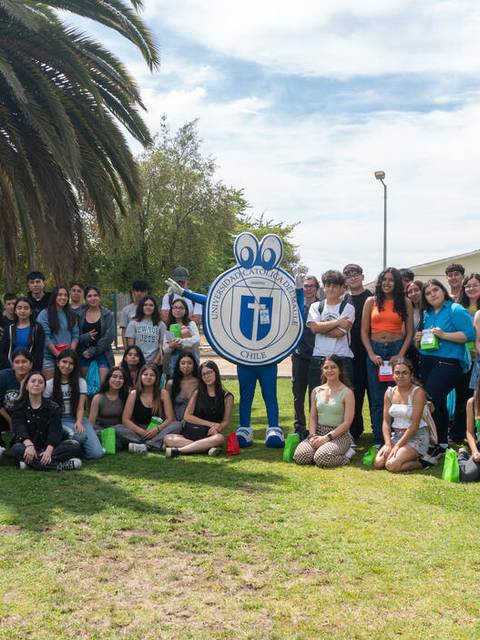 Un grupo grande de personas posa en un jardín con palmeras y un personaje de dibujos animados.