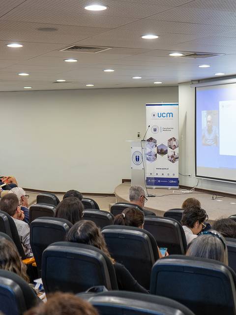 Una conferencia en un auditorio con una audiencia atenta y una presentación en pantalla.