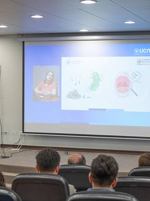 Una presentación en una sala con una pantalla mostrando gráficos y una conferencista en el fondo.