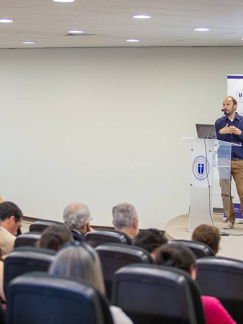 Un hombre presenta frente a una audiencia en un salón de conferencias.